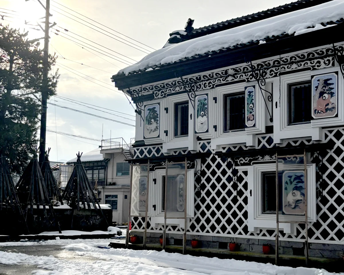 雪景色の中に佇む旧機那サフラン酒製造本舗の鏝絵蔵