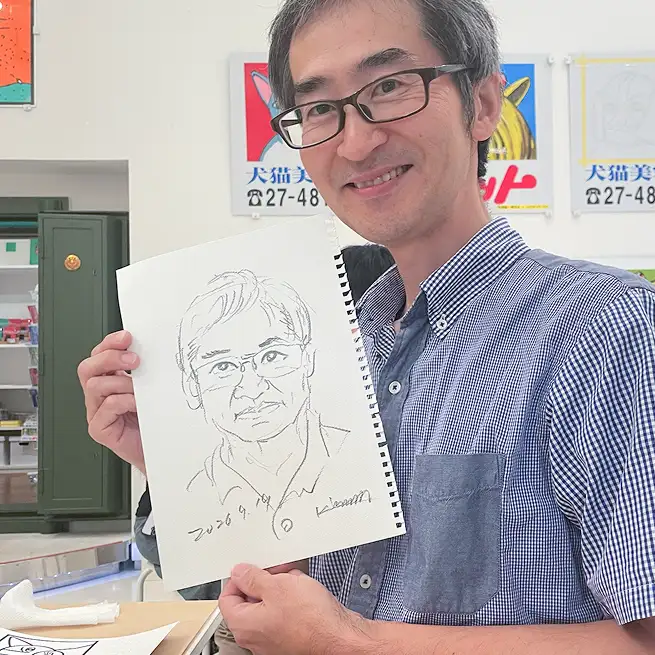 青柳謹一さんが描いたconnieさんの似顔絵を持つconnieさん